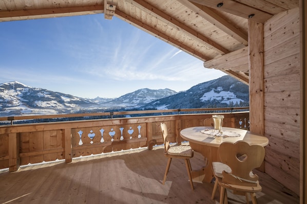 Une terrasse en bois avec une table et des chaises, offrant une vue sur des montagnes enneigées.