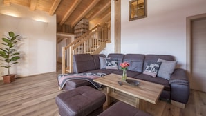 A cozy living room with a wooden ceiling, a large sofa with multiple cushions, a coffee table, and a potted plant.