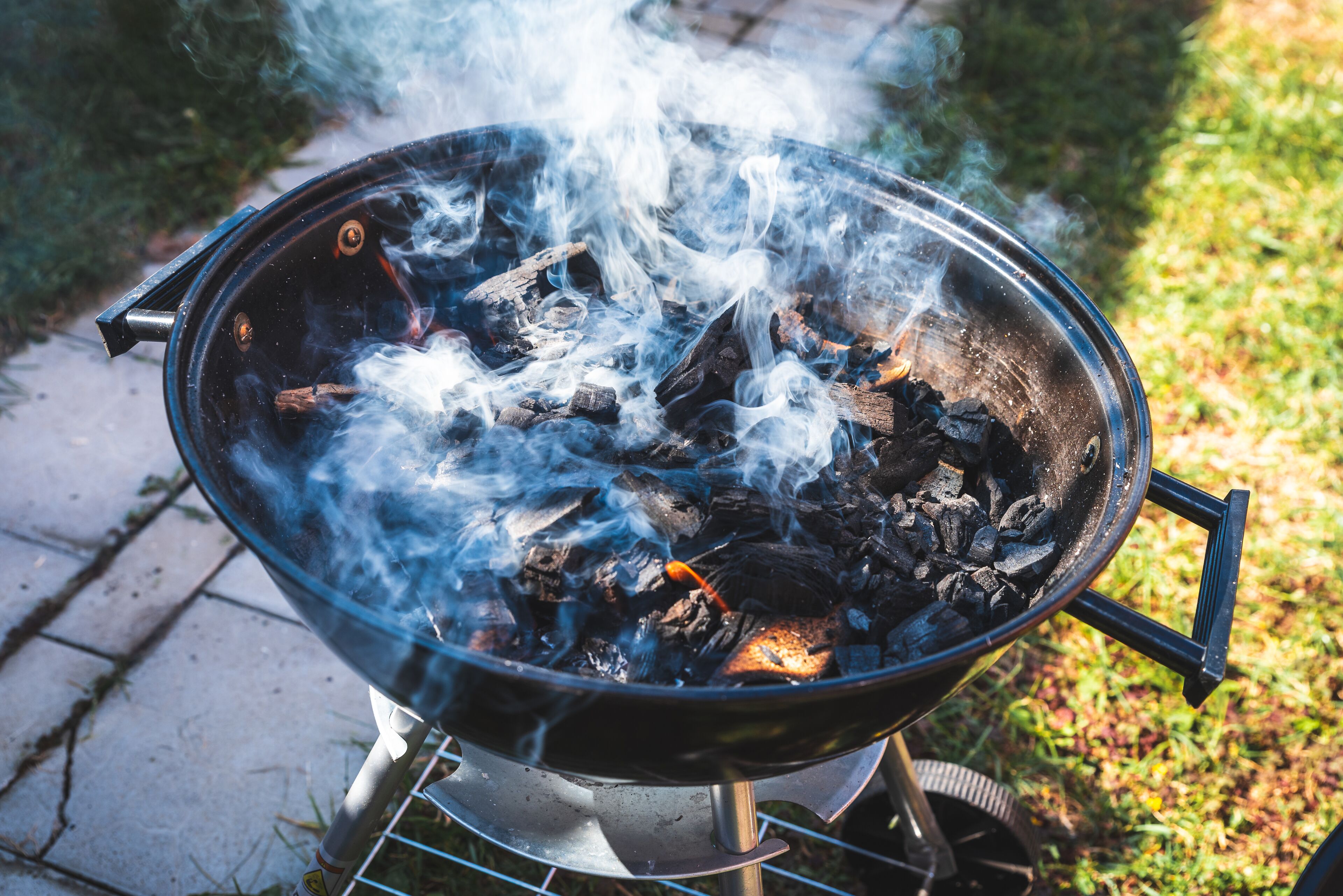 A portable grill with visible charcoal and smoke, placed on a metal stand outdoors.