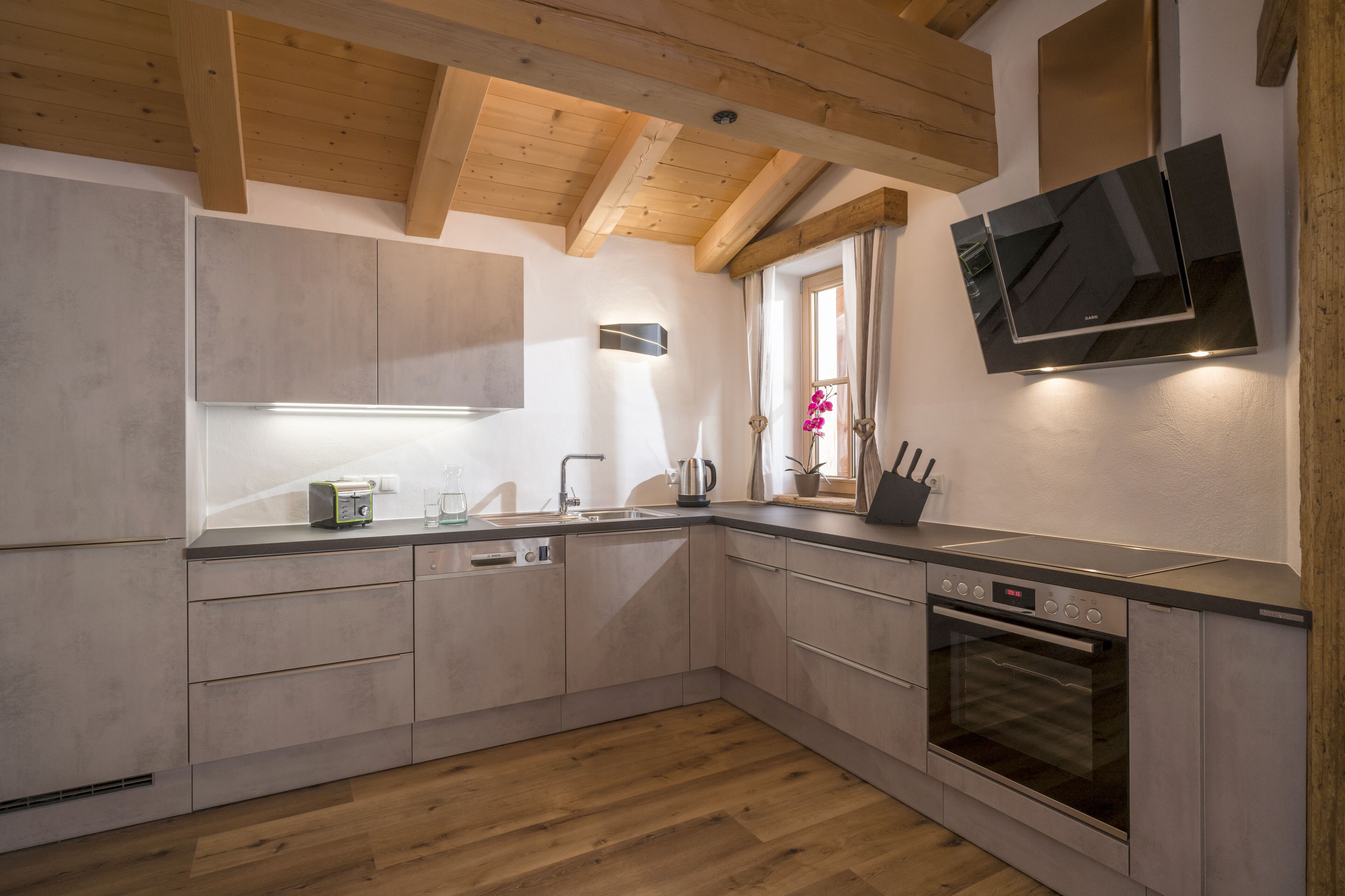 Une cuisine moderne avec des poutres en bois, un four encastré et un téléviseur fixé au mur.