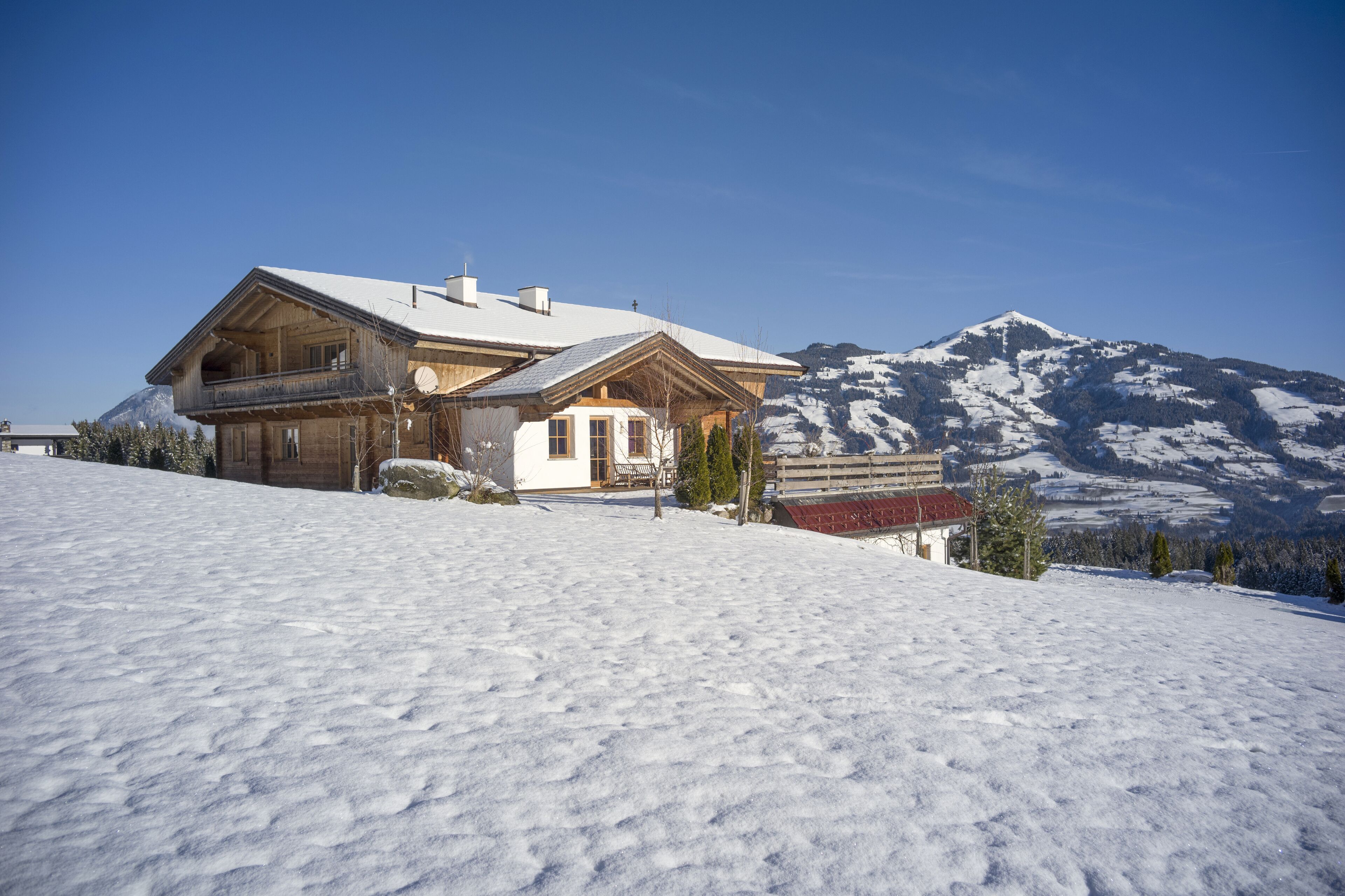 Eine Holzhütte mit Balkon, vor einer verschneiten Berglandschaft.