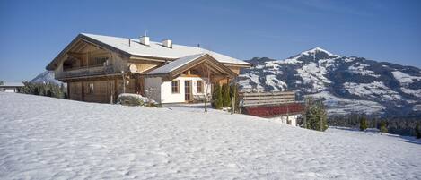 Eine Holzhütte mit Balkon, vor einer verschneiten Berglandschaft.