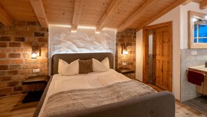A cozy bedroom with a wooden ceiling, a brick wall, and a large bed with white bedding.