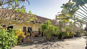 A yellow building with a tiled roof, surrounded by various plants and trees. - Jero Harum Homestay (Tabanan)