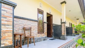 A building with a stone facade, a wooden chair, and a tiled entrance area. - Jero Harum Homestay (Tabanan)