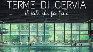 Ein Schwimmbad mit Blick auf Bäume durch große Fenster, und der Schriftzug "TERME DI CERVIA il sale che fa bene" ist sichtbar.