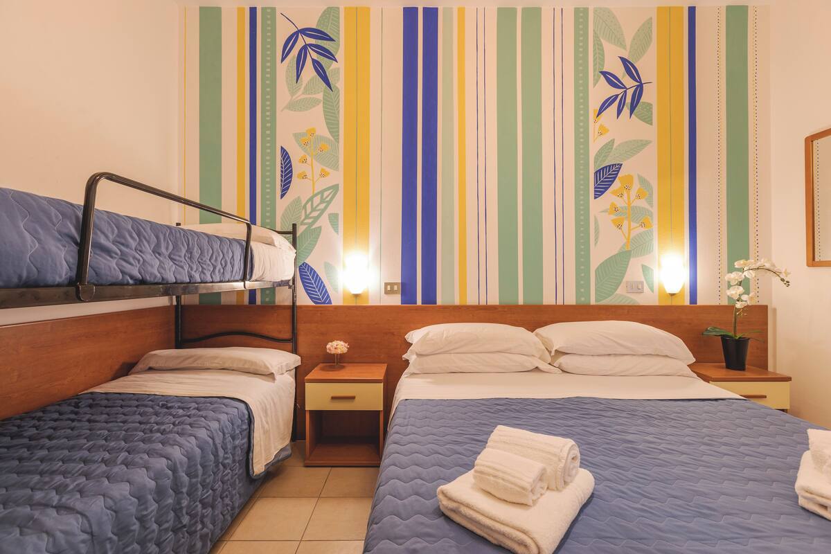 Une chambre d’hôtel avec un lit superposé, un lit simple et une table de chevet avec une lampe.