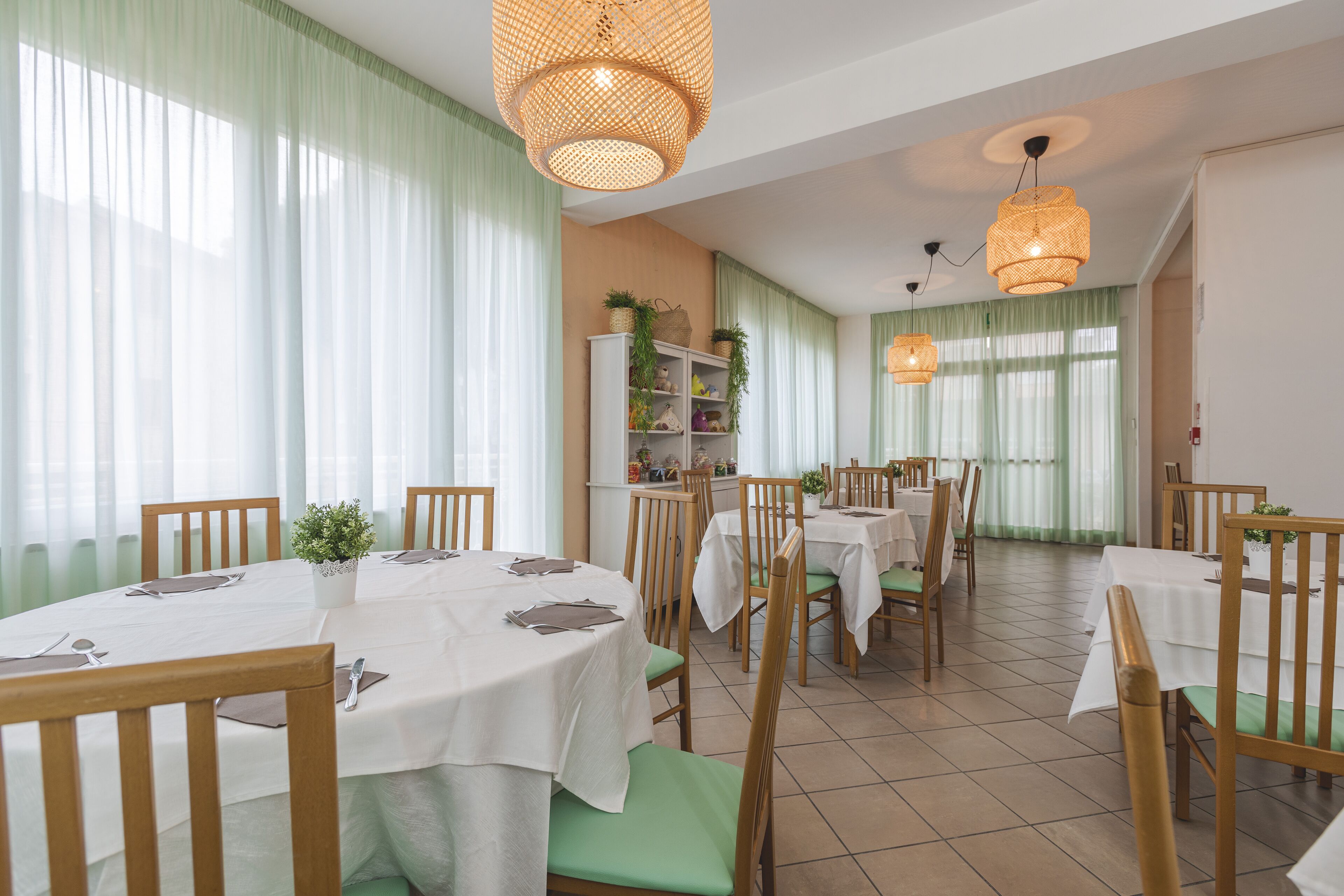 A dining area with round tables, green cushioned chairs, and wicker pendant lights.
