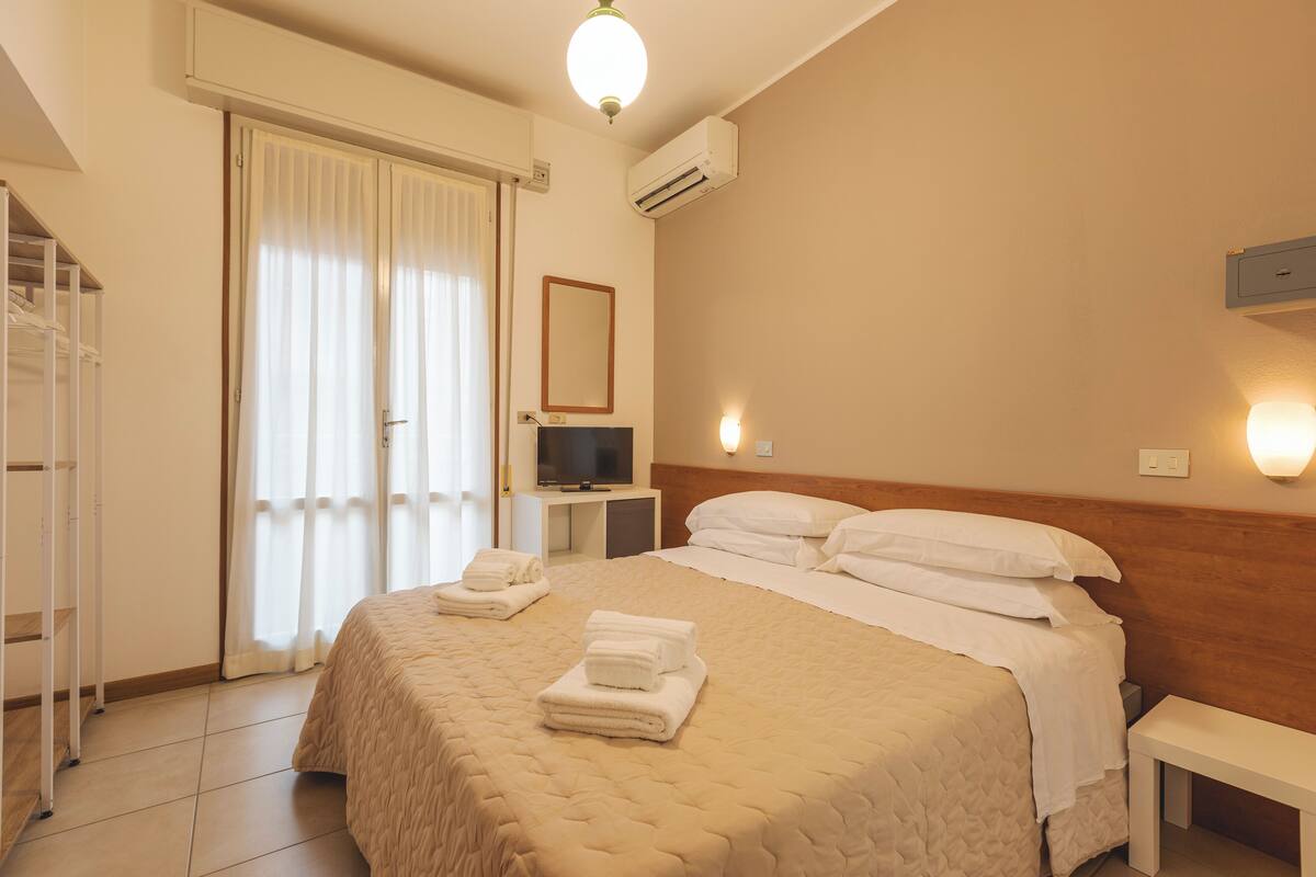 Une chambre d’hôtel avec un lit, une télévision, une table de chevet et une fenêtre avec des rideaux.
