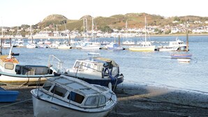 A harbor with several boats docked, a sandy shore, and a town in the background. - 50A Lloyd Street West (Llandudno)