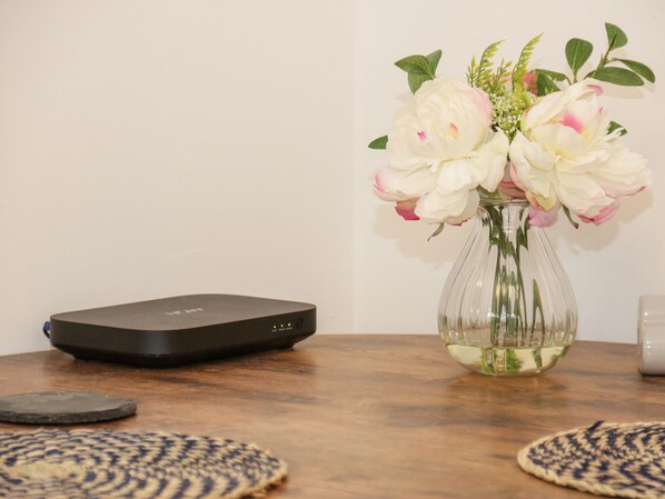 A table with a black electronic device, a vase with white flowers, and two woven placemats.