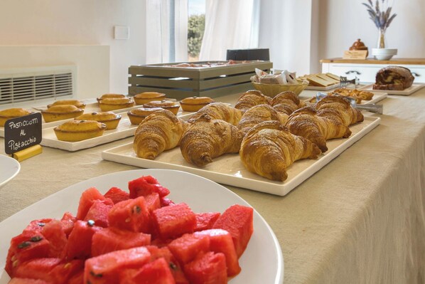 A buffet table with pastries, croissants, and watermelon.