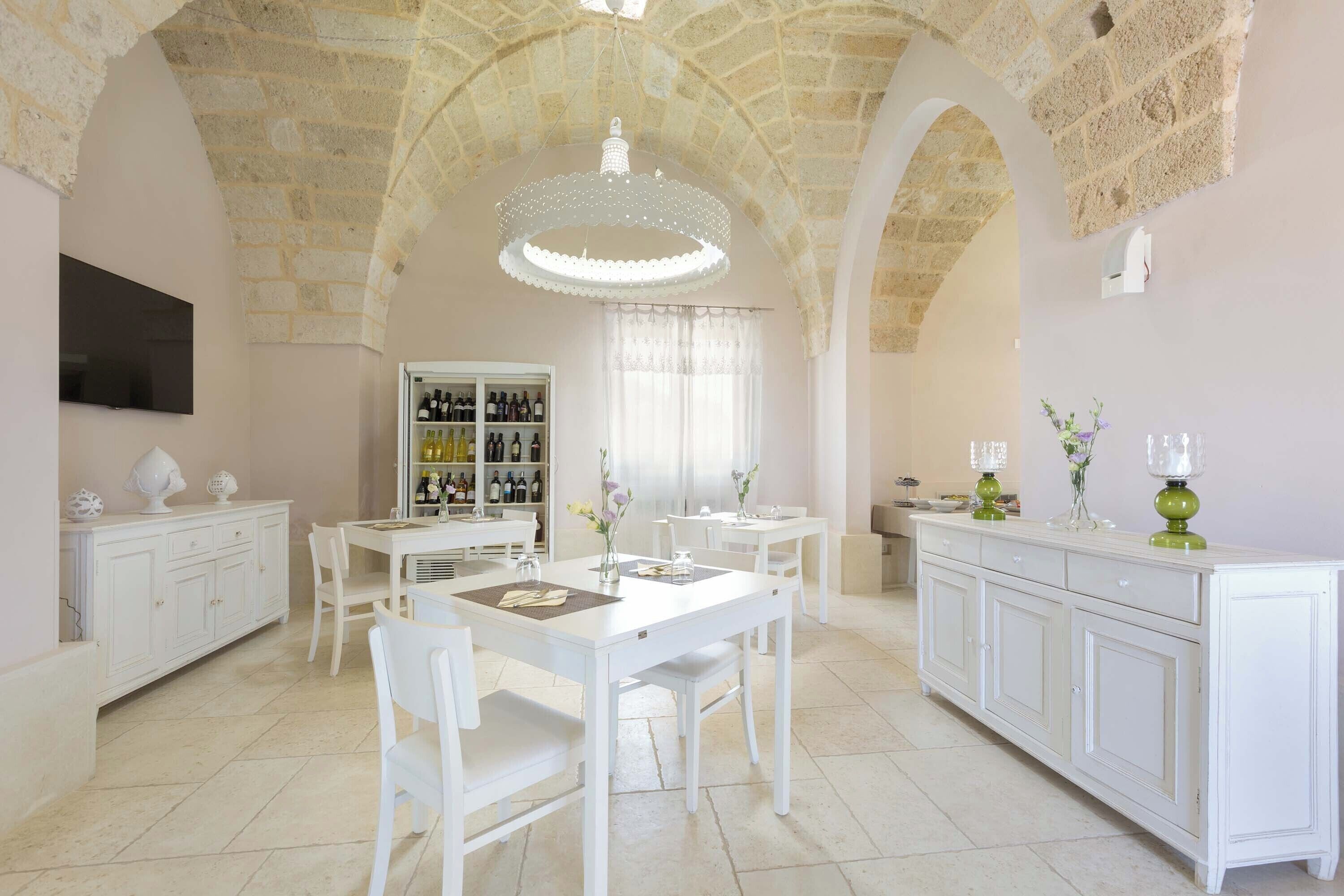 A spacious dining area with white furniture, a wine rack, and a chandelier.