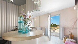 Ein modernes Interieur mit einer gewölbten weißen Arbeitsplatte, einer Vase mit Blumen und Blick auf einen Außenbereich mit einem Pool.