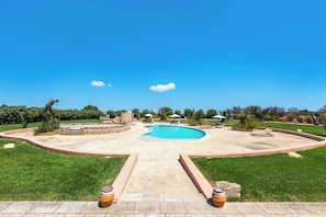 Un jardin avec une piscine, une terrasse en pierre et une pelouse.
