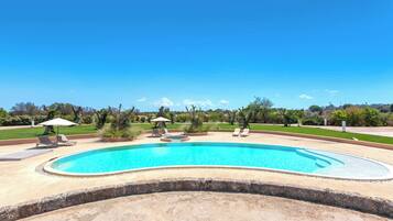Relax by the oval-shaped pool surrounded by lounge chairs and umbrellas, set amidst a serene landscape with neatly trimmed bushes and trees.