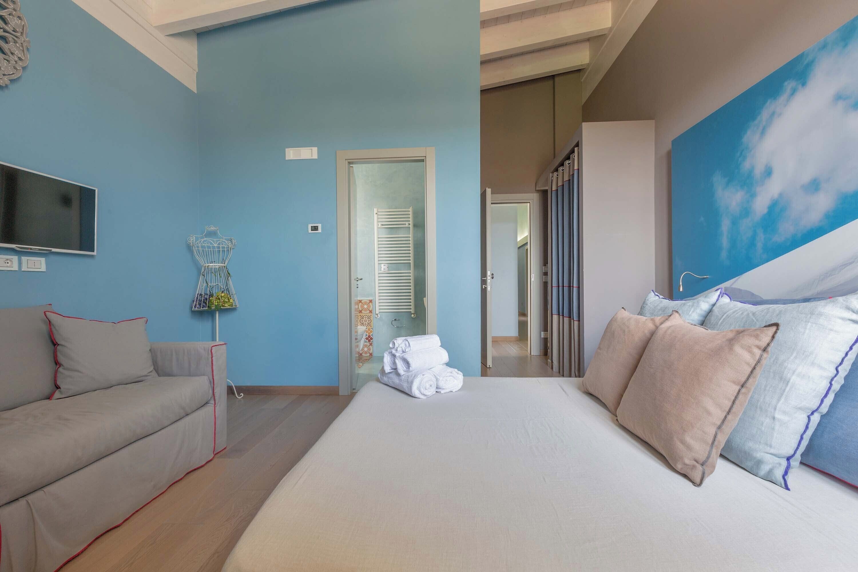 Un dormitorio con una cama grande, un sofá, un televisor y un cuadro de un cielo.
