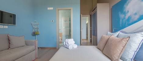 Un dormitorio con una cama grande, un sofá, un televisor y un cuadro de un cielo.
