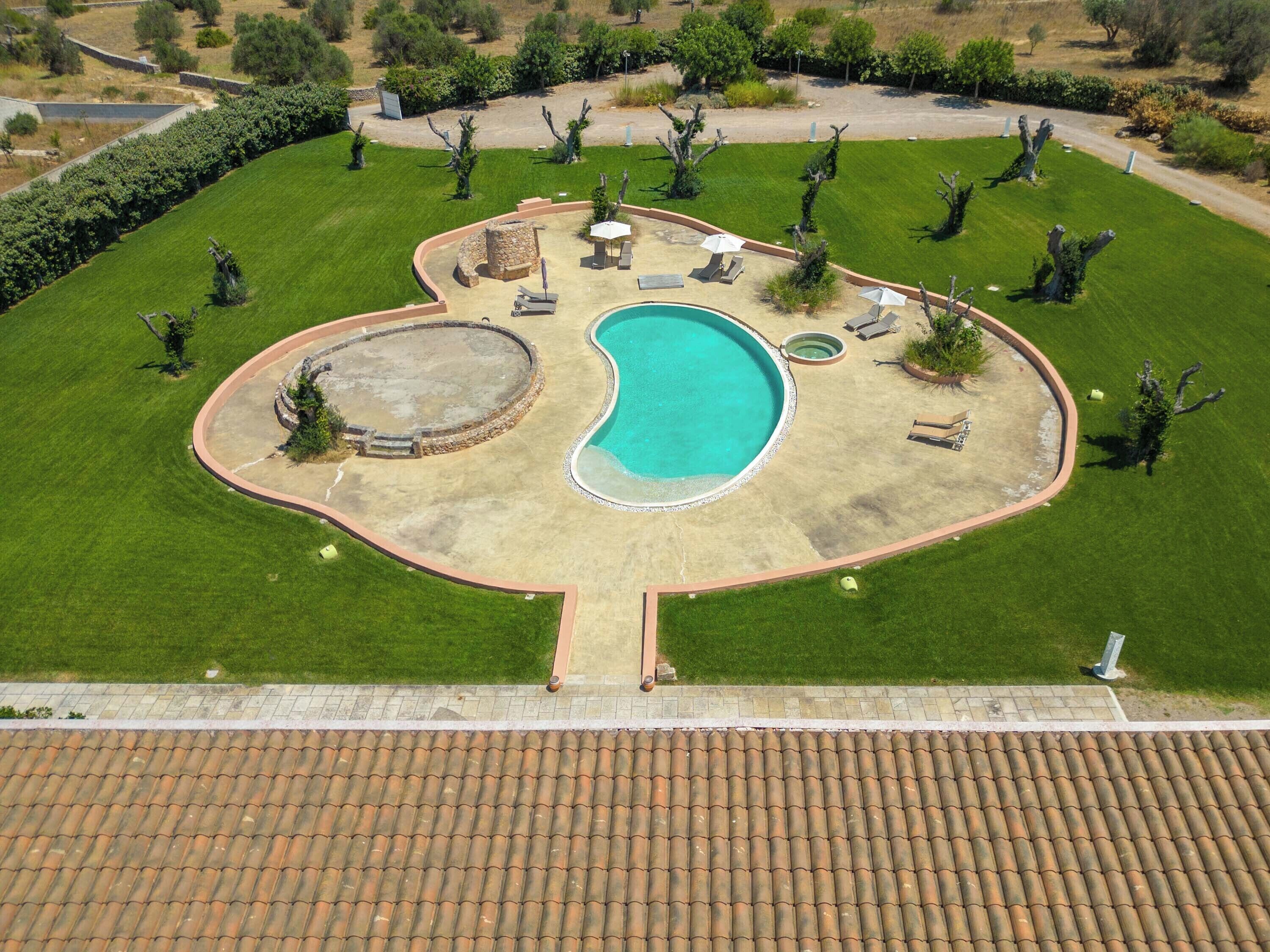 An aerial view of a landscaped property with a swimming pool, lounge chairs, and a stone structure.