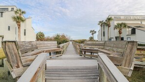 Une promenade en bois mène à une zone de plage bordée de bâtiments des deux côtés.