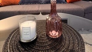 A living room with a grey sofa, orange and blue pillows, a glass vase with yellow flowers, and a white candle labeled "Home Fragrance Pink Vanity & Rosewater." - 2 room apartment in a historic building in the old town of Goslar (Goslar)