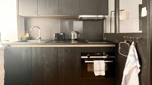 A modern kitchen with dark cabinets, a wooden floor, and a built-in oven. - 2 room apartment in a historic building in the old town of Goslar (Goslar)