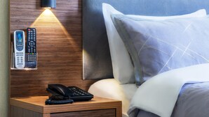 A hotel room with a wooden nightstand, a phone, and a remote control.
