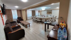 A hotel room with a living area, a dining table set for a meeting, and a minibar with bottled water.