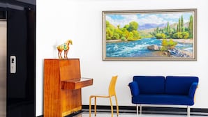 A reception area with a wooden desk, a blue sofa, a chair, and a painting of a river landscape.