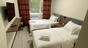 Une chambre d’hôtel avec deux lits, un bureau, une chaise, une télévision et une fenêtre avec des rideaux.
