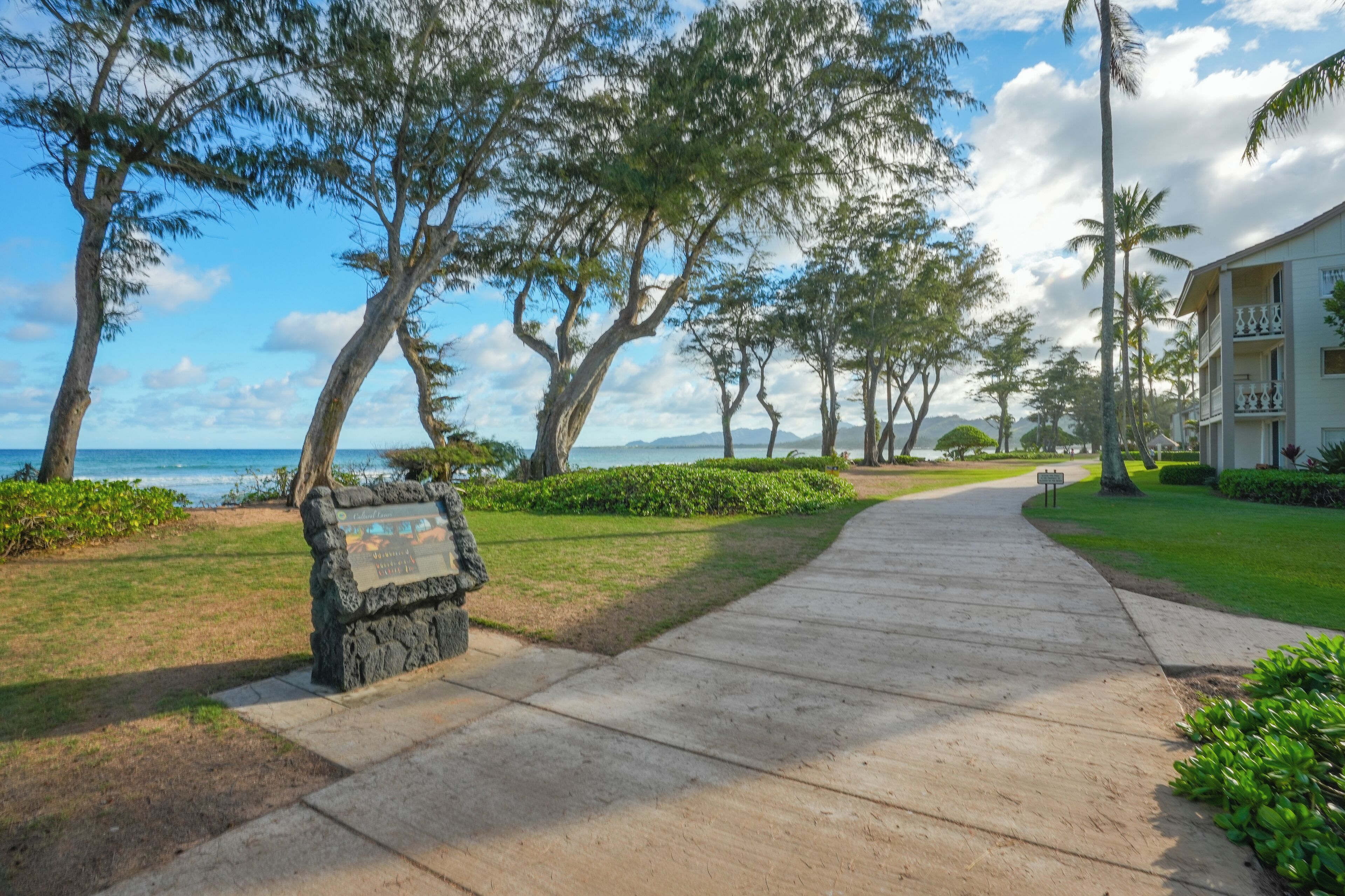 A pathway leading to a building with a view of the ocean and trees.
