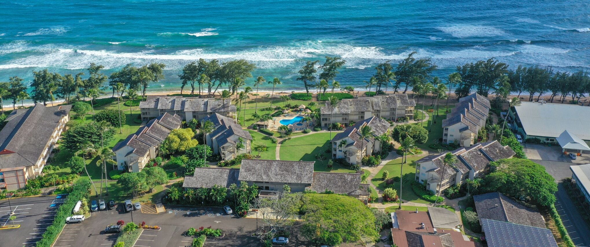 An aerial view of a coastal resort with multiple buildings, a swimming pool, and a parking area.