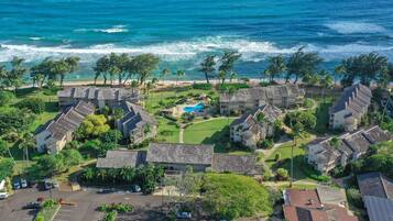 An aerial view of a coastal resort with multiple buildings, a swimming pool, and a parking area.