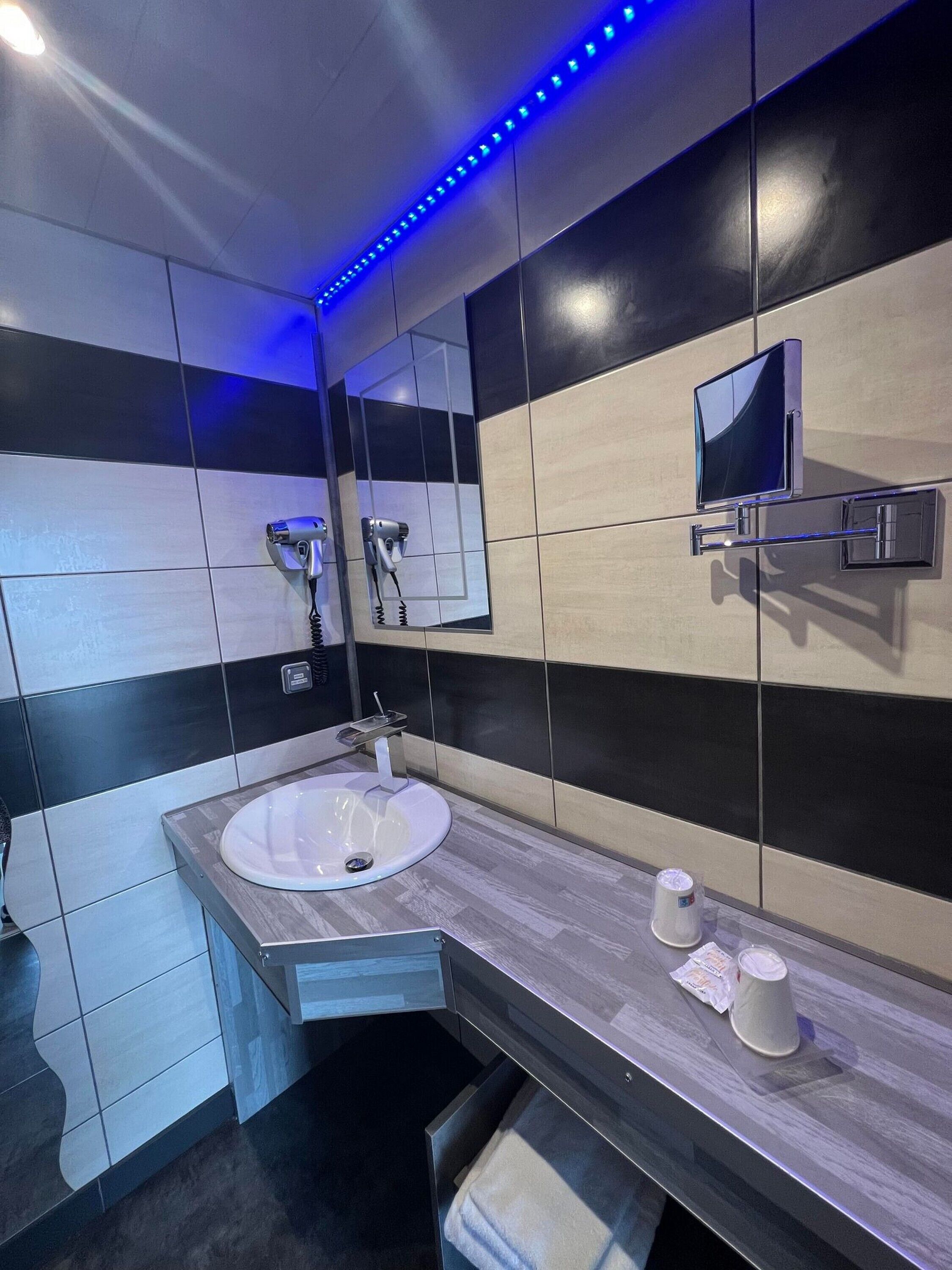 A modern bathroom with a large mirror, a sink, and a television mounted on the wall.