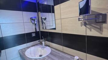 A modern bathroom with a large mirror, a sink, and a television mounted on the wall.