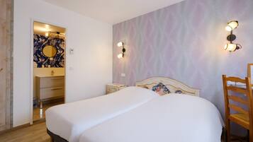 A bedroom with a large bed, a wooden chair, a nightstand, a wall-mounted light fixture, and a mirror with a floral design.