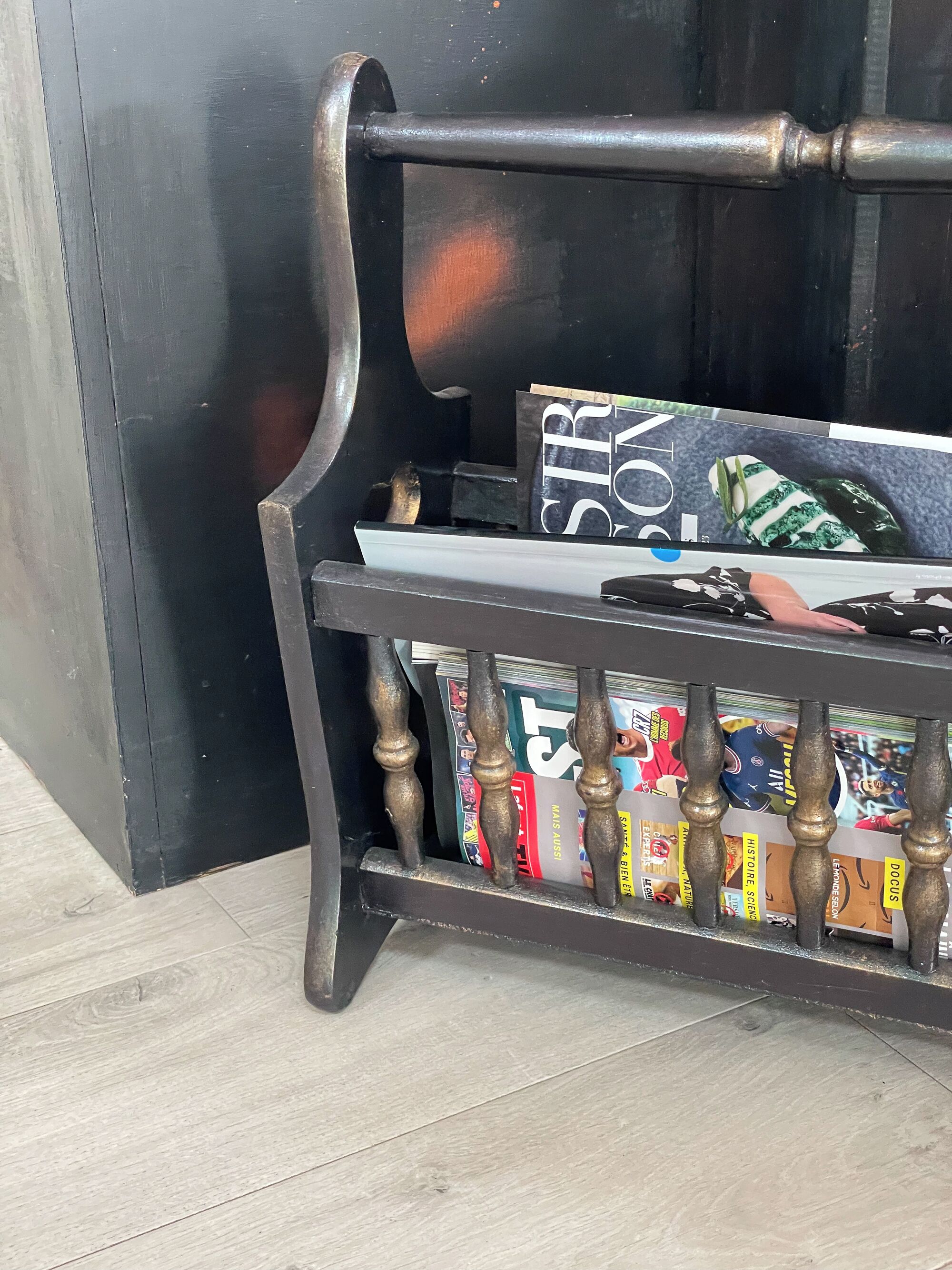 A magazine rack with multiple magazines, a black wall, and a tiled floor.