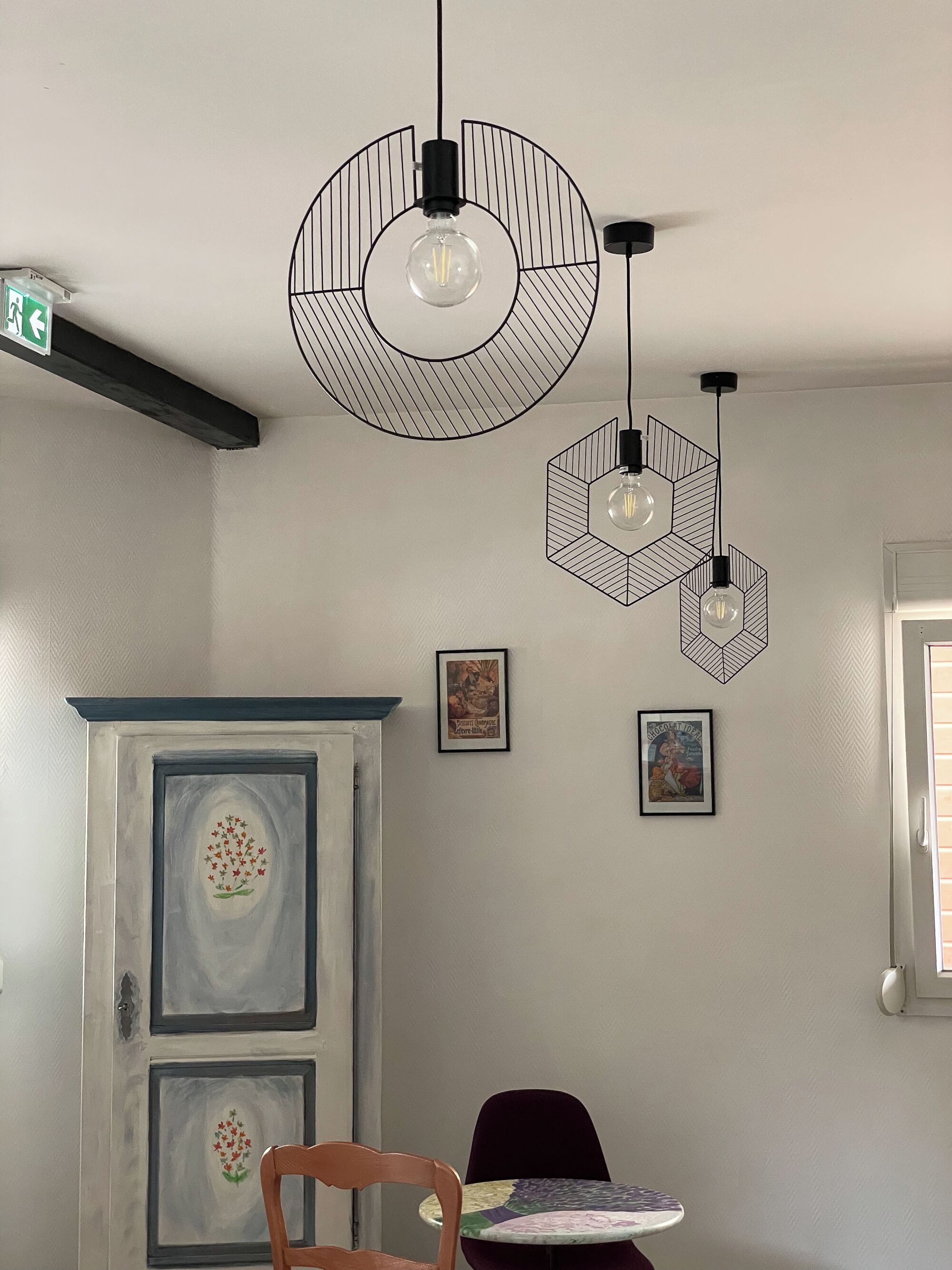 Una habitación con una puerta blanca, una silla de madera, una mesita pequeña y tres lámparas colgantes con diseños geométricos.