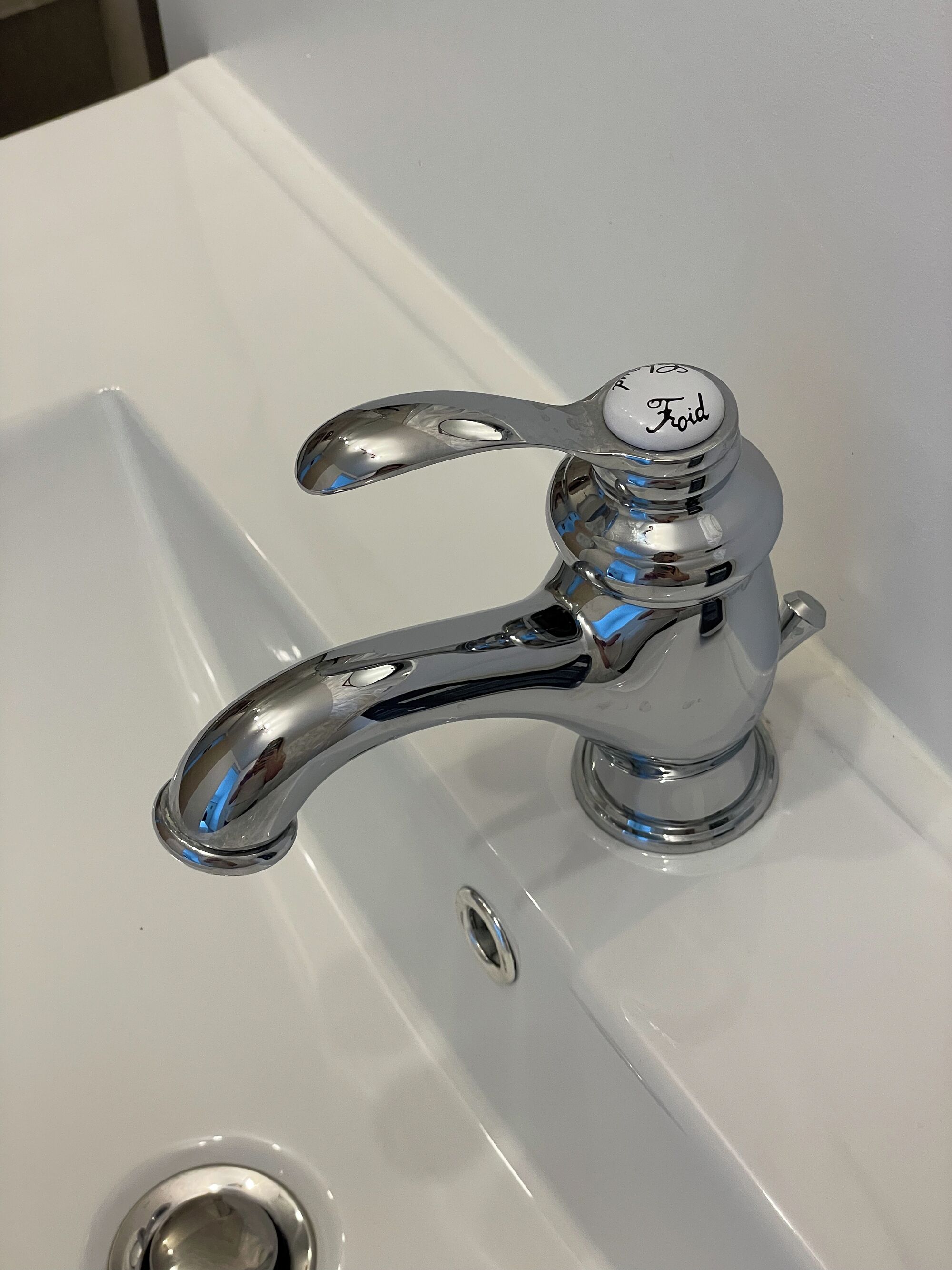 A chrome faucet with a lever handle and a control knob labeled "Foil" on a white sink.