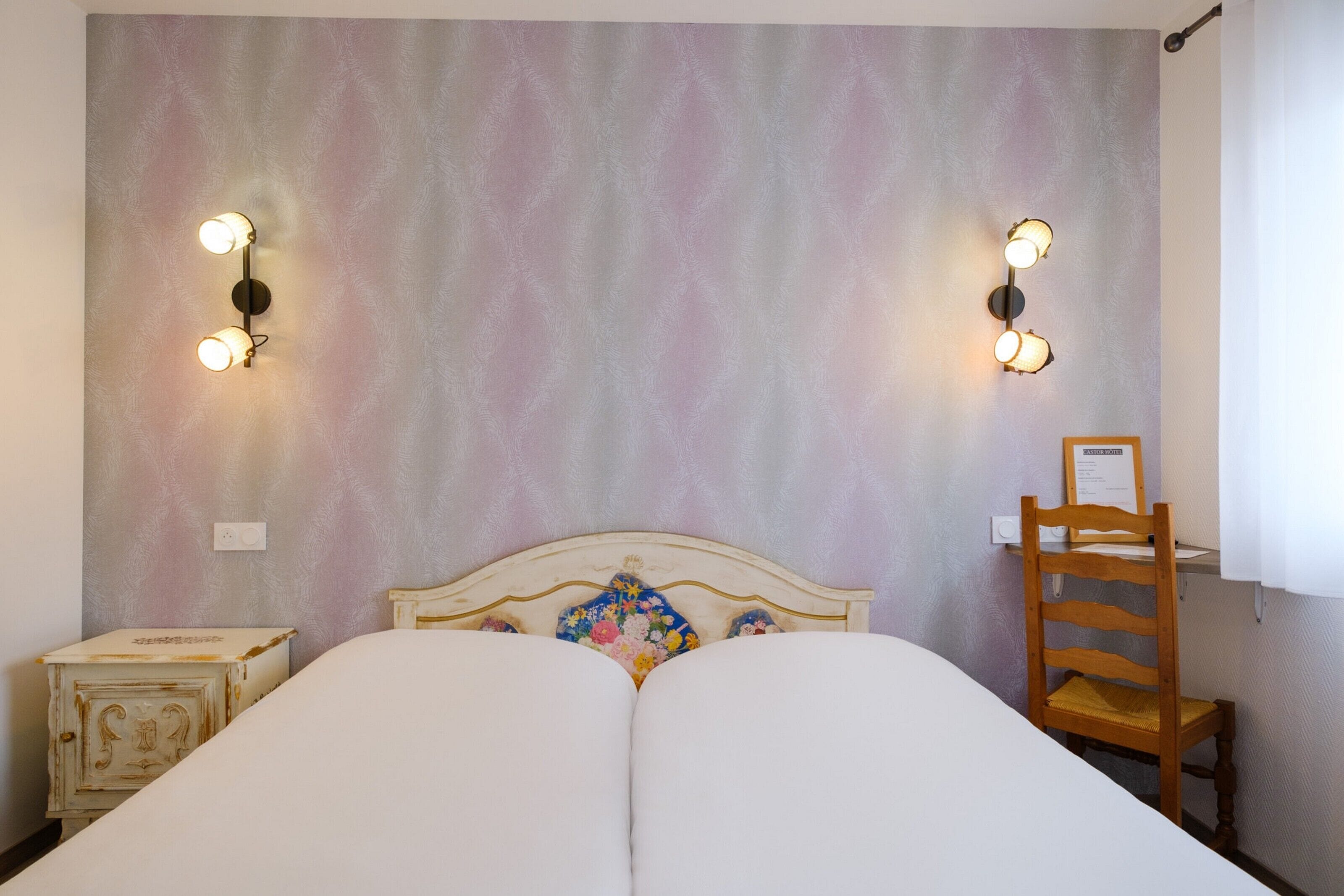 A bedroom with a double bed, a wooden chair, and two wall-mounted light fixtures.