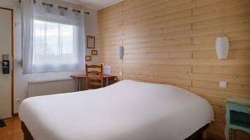 A bedroom with a large bed, a wooden wall, a small table, and a chair.