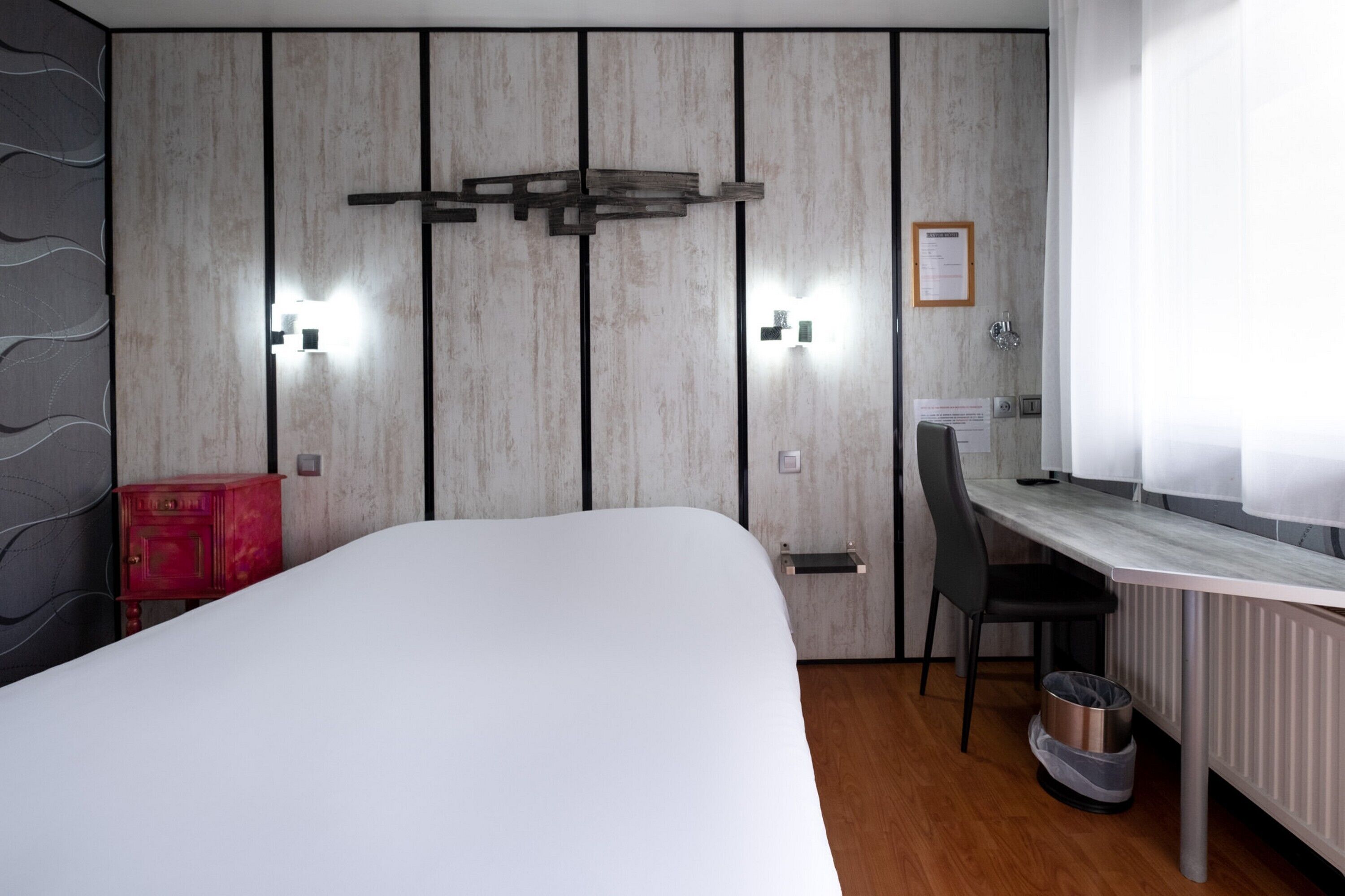 Ein Schlafzimmer mit Bett, Schreibtisch und Stuhl. Darunter befindet sich ein Heizkörper und neben dem Stuhl ein Mülleimer.