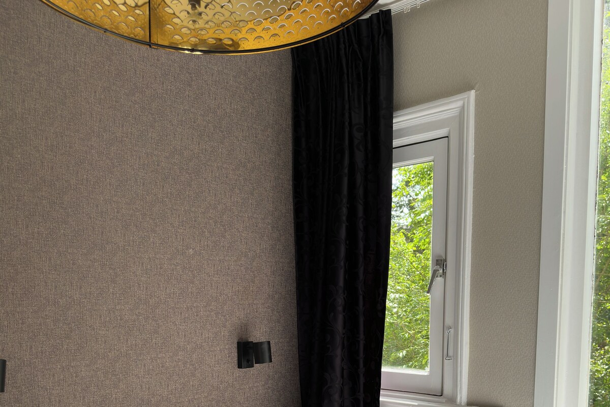 A bedroom with a bed, two pillows, a window with a view of greenery, and a textured wall.