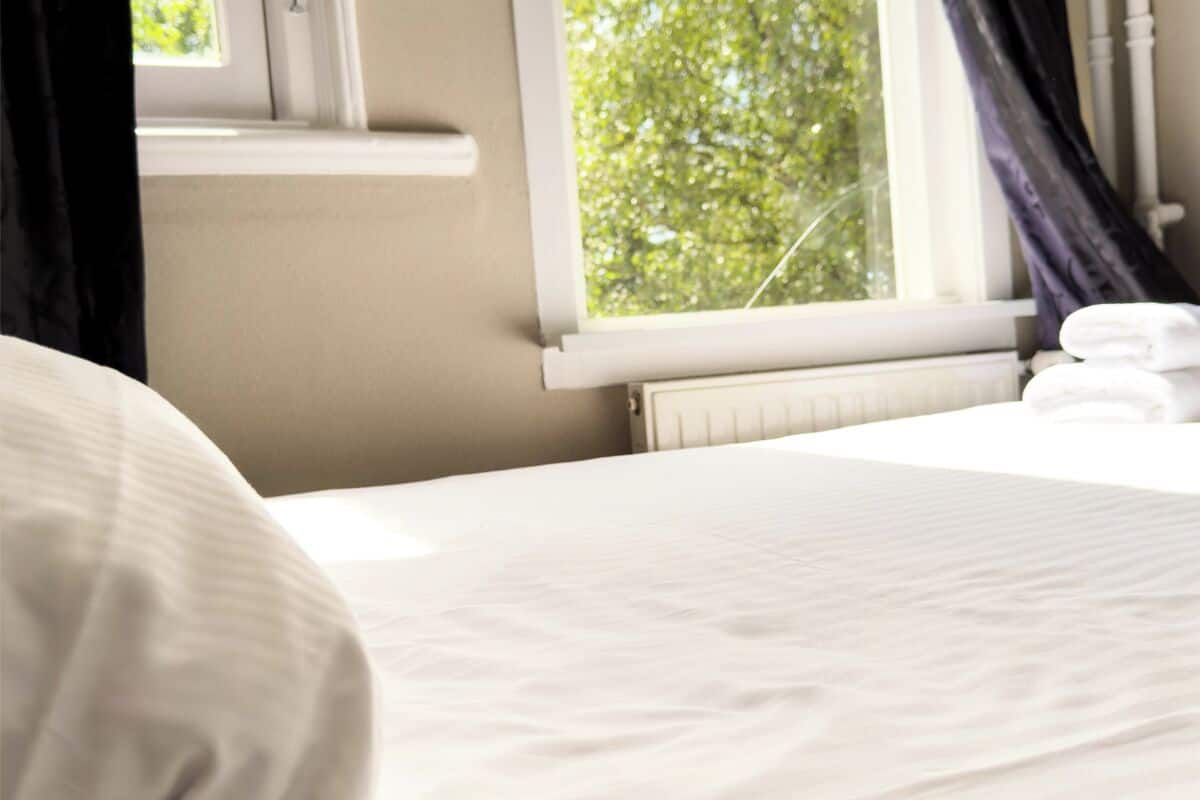 A hotel room with a bed, a window with curtains, and a radiator.