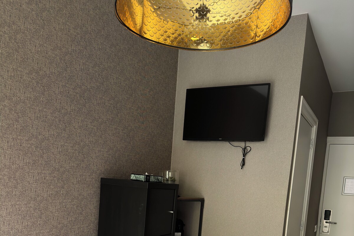 A bedroom with a bed, a wardrobe, a TV mounted on the wall, and a door leading to another room.