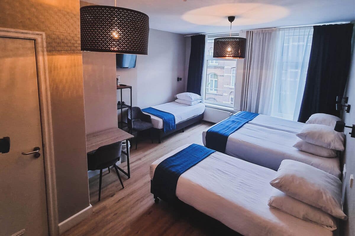 A hotel room with two beds, a desk, a chair, a TV, and a window with curtains.