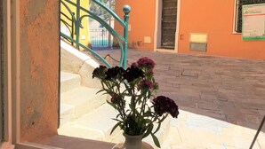 A window view of a building with a vase of flowers on a windowsill and a blue glass on the floor.