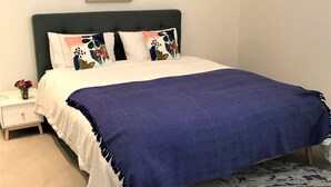 A bedroom with a bed, pillows, a nightstand, a vase with flowers, and a poster on the wall.