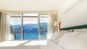 Et hotelværelse med en stor seng, udsigt til en sø og bjerge, samt en skydedør.