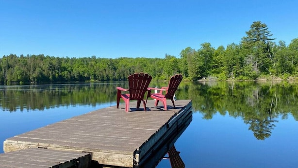 Un moll de fusta que s'endinsa en un llac tranquil, amb dos cadiretes Adirondack vermelles a sobre.